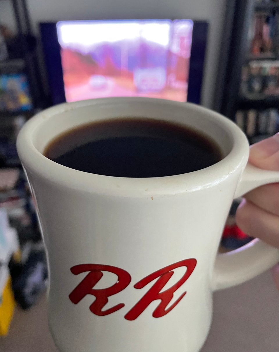 A large cup of coffee held in front of a tv playing twin peaks