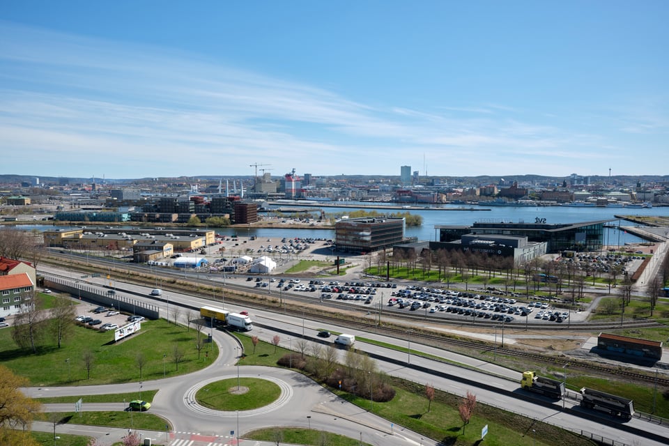 A view of Göteborg from a high point. In front, there are roads and a roundabout. Further away, there's a river and beyond it the silhoutte of the city center.