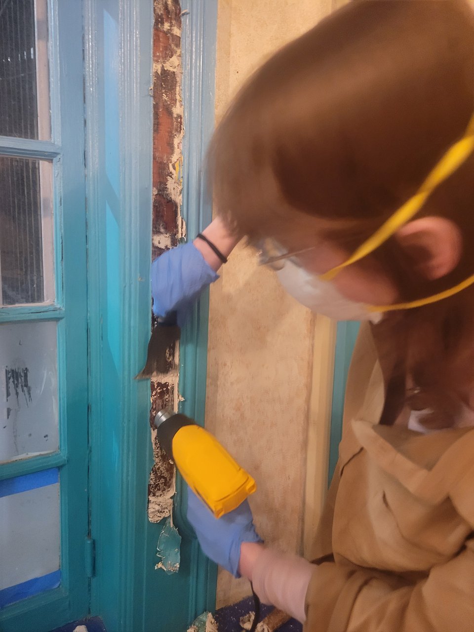 A friend scraping layers of paint off the wooden windows of the bar using a heat gun and scraper.