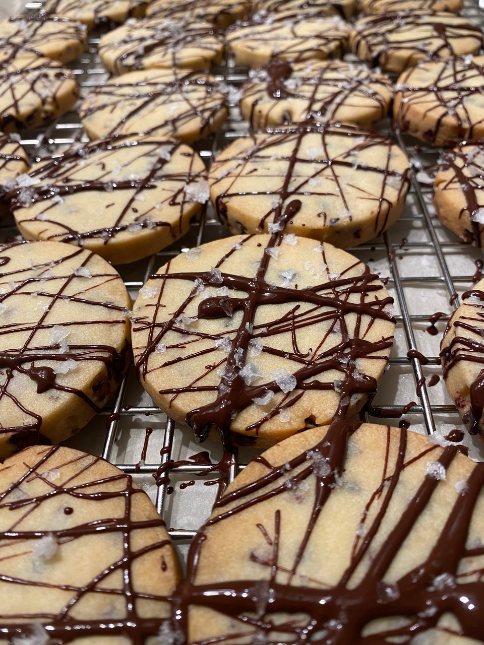 Light brown round shortbread cookies splattered with chocolate and flaked with salt.