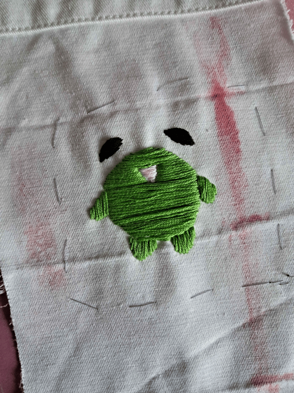 Picture of an embroidery attempt of a small green frog on some scrap fabric