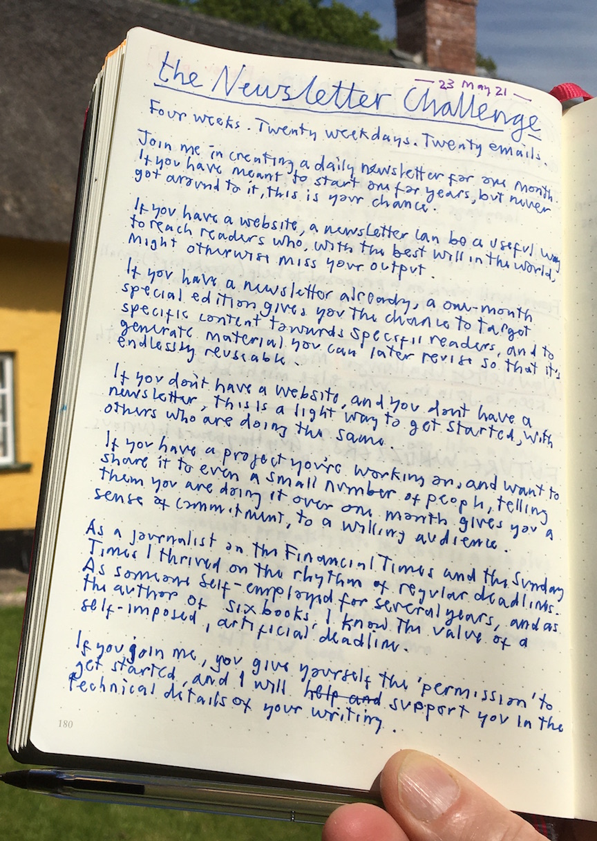 Photo of a page of handwritten text in a notebook, held up for the camera in sunshine in what could be a garden. Text invites people to join the Newsletter Challenge