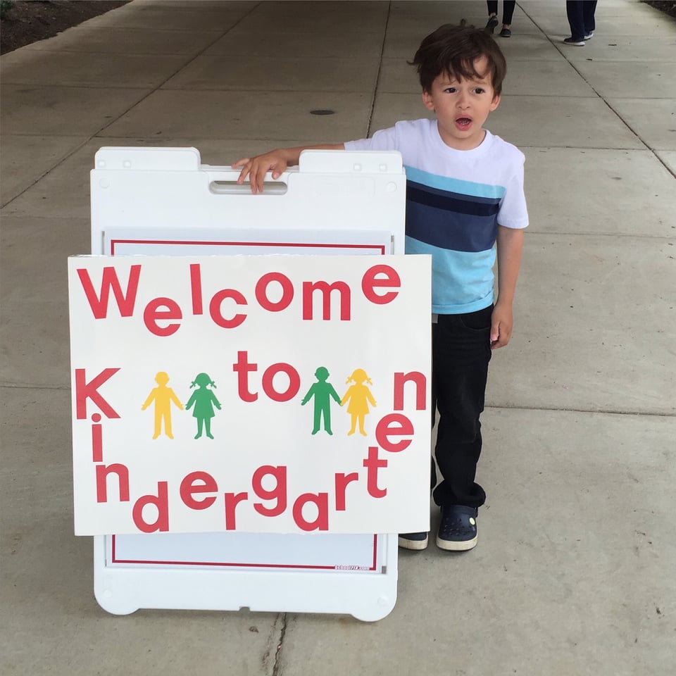 a child stands beside a sign saying Welcome to Kindergarten