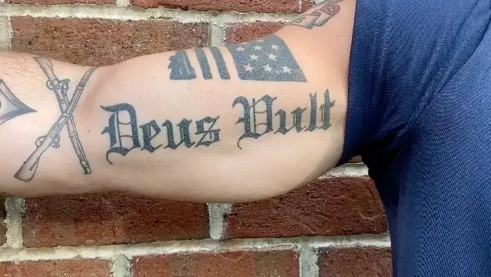 right forearm tattoo of an asshole saying "deus vult"