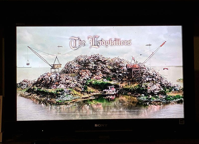 A photo of my television, which in this instant displays the title of the movie The Ladykillers over a trash barge.