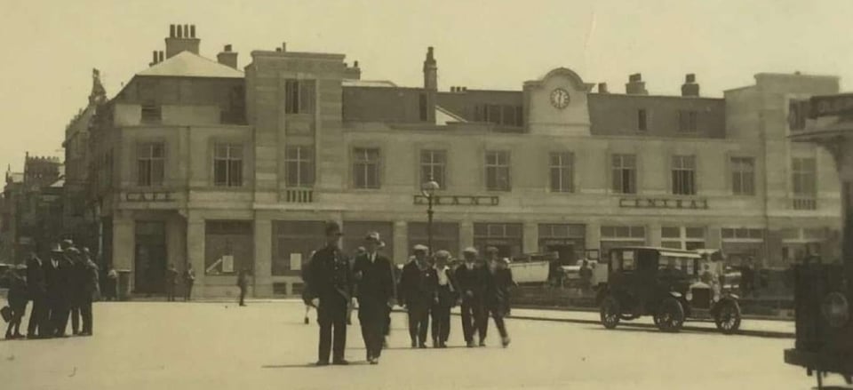 A 1920s or early 1930s photo of the Grand Central Hotel. It has two storeys. The ground floor is plate glass windows, then the upper floor has nice crittall frames. There are two short towers either side of a clock on a large pediment.