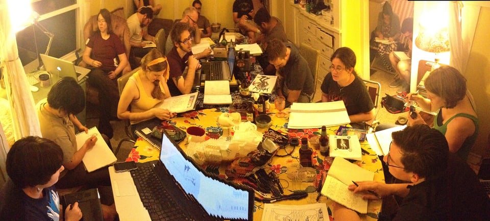 A huge gaggle of cartoonists crammed around a dining room table.