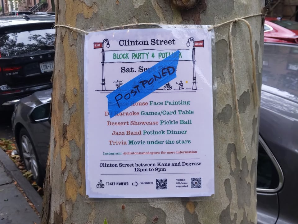 A sign tied to a tree indicating that a Clinton Street (Brooklyn) Block Party and Potluck is set to take place. However, a blue piece of tape with POSTPONED on it covers the date.
