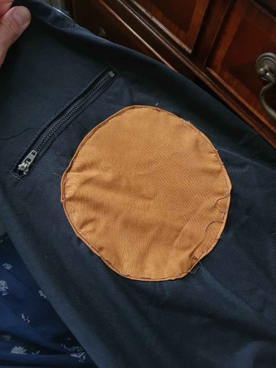 The chest of the black apron with a large orange fabric circle sewn onto it to cover the logo. The seams are uneven and the circle is slightly misshapen.