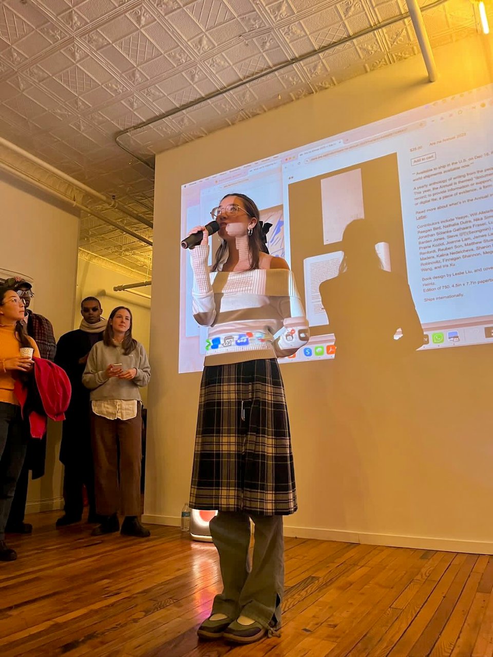 Maya with a mic in front of a projected Are.na channel.