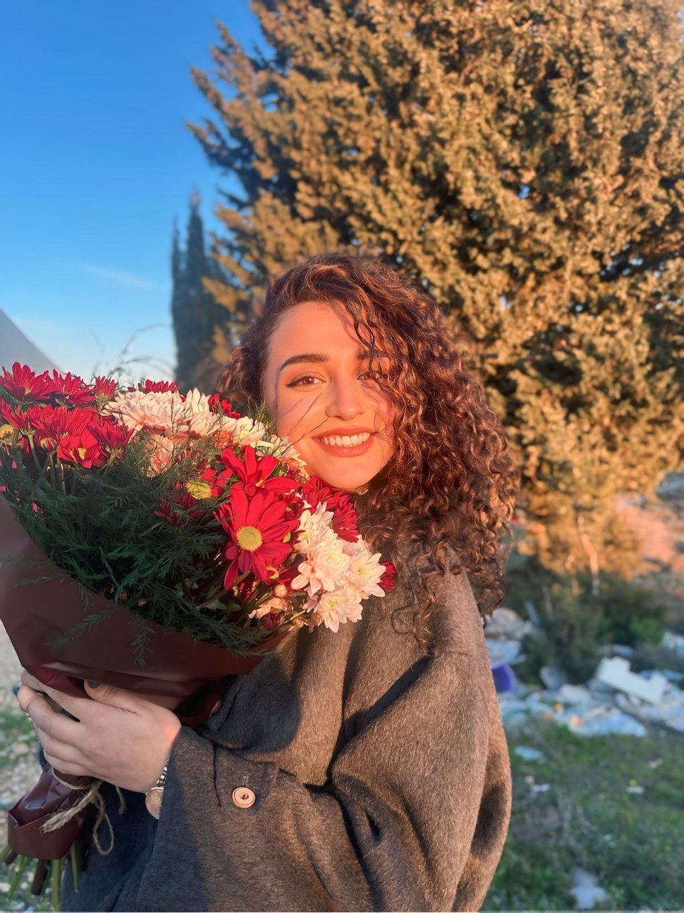 A beautiful young woman with long brown curly hair, holding a bouquet of flowers
