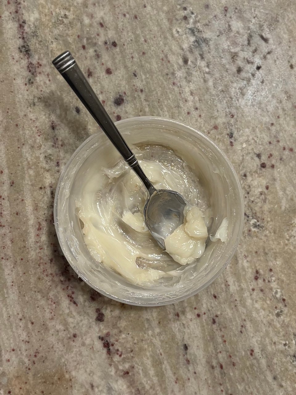 A small deli container with pork fat and a spoon.