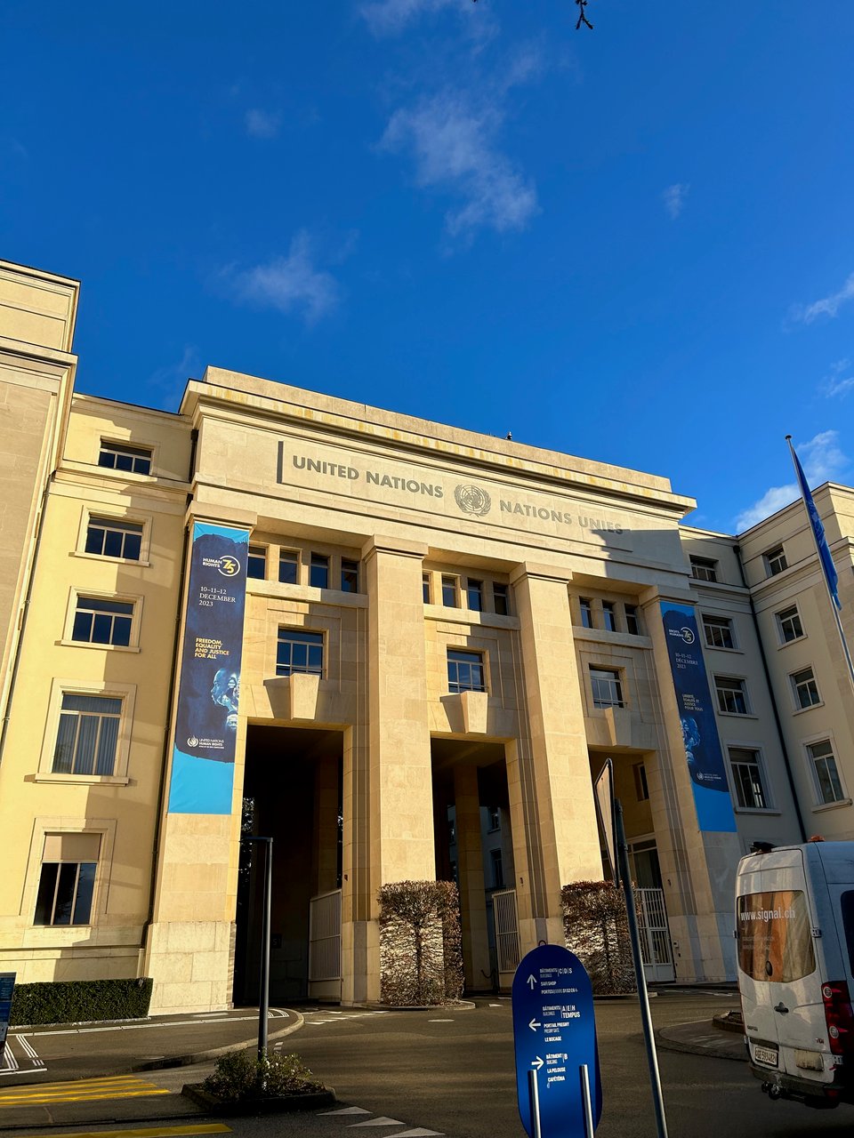 A photo of a tall, imposing building lit in the morning sun. At the top of the building it says "United Nations Nations Unites"