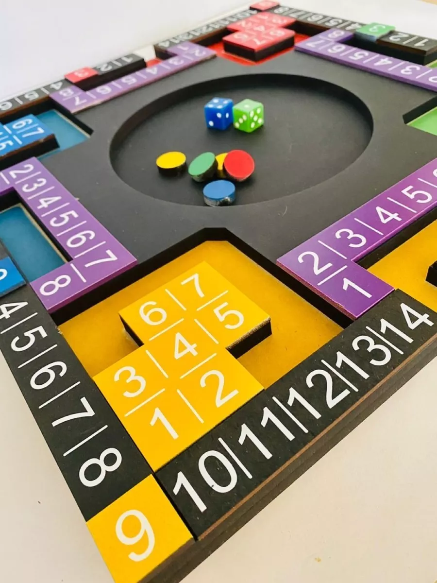 A picture of a poleana game board. It is made of wood that is painted, primarily black, with sections in bright yellow, pink, green, red, and blue. All around the edge of the square are squares with numbers ranging from 1 to 14. There are several round counters in the center of the game board, and two dice.