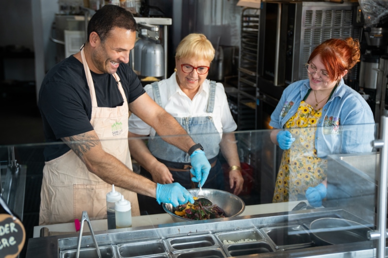 a person serving food on a line in a restaurant as two others watch