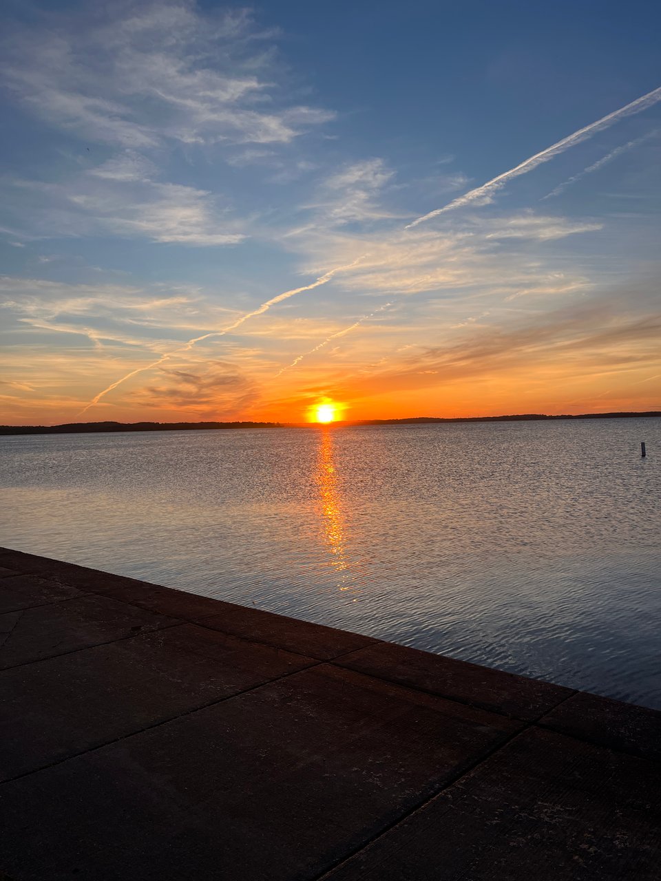 orange sun setting right on the horizon above the lake and concrete walkway