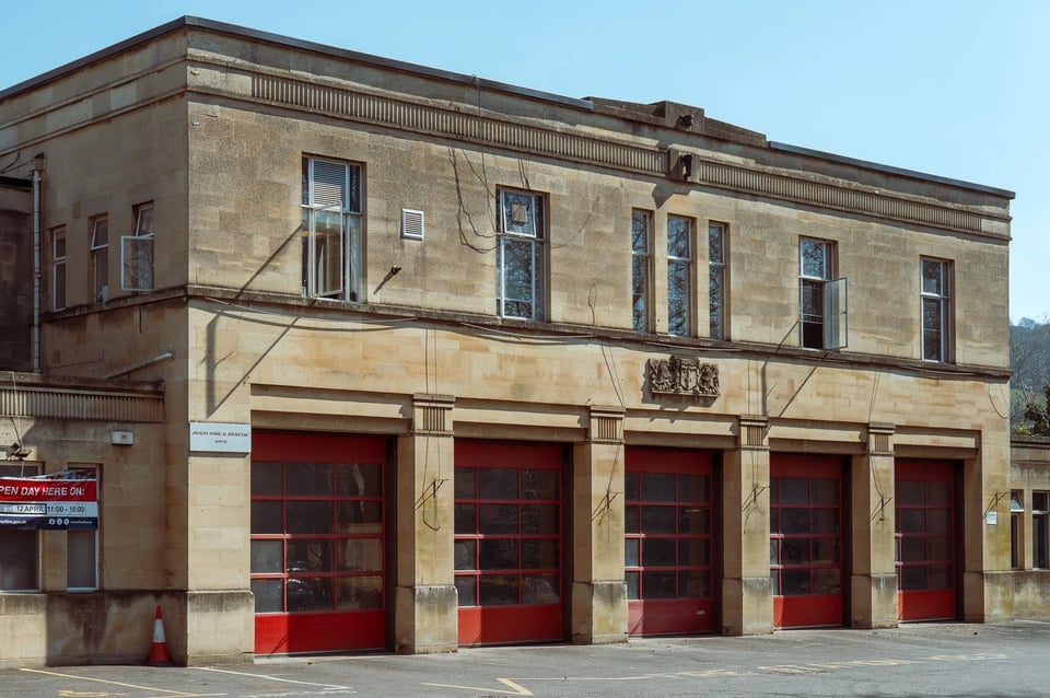 A simple fire station clad in Bath stone. There are five engine bays set into it, with red doors. On the floor above, metal framed windows have been set into it and a crest set into the wall. Classical elements in the pediment and around the bays hints as classicism but are exceptionally stylised into nothing more than lines.