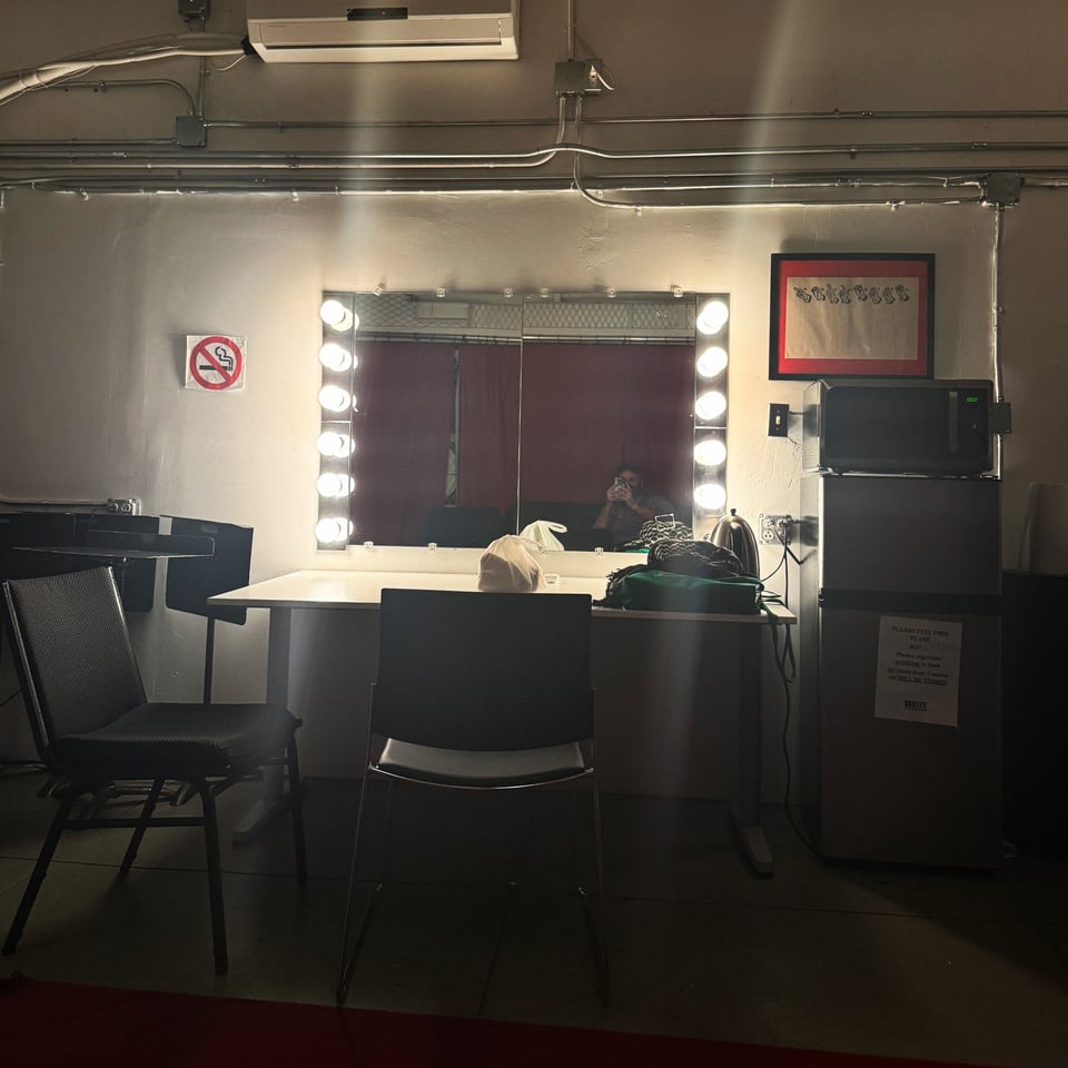 a vanity mirror, a few chairs, and a refrigerator backstage at a music venue