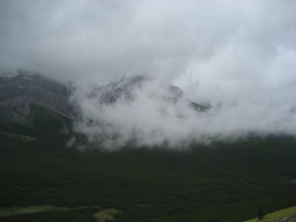 A green mountain pokes up into heavy cloud cover.