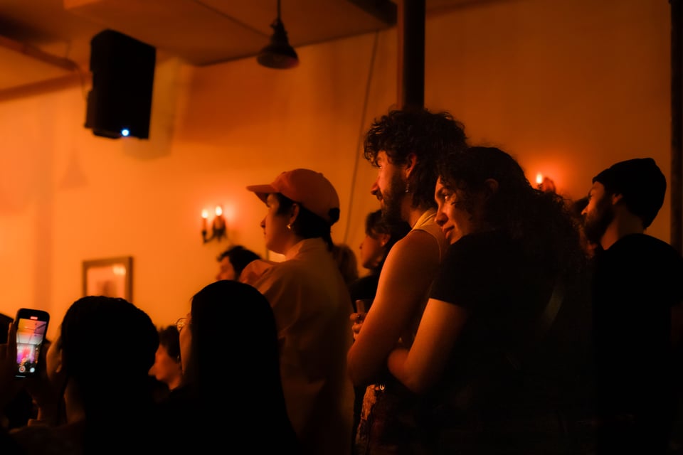 victoria and leche hug while watching a show, bathed in yellow light
