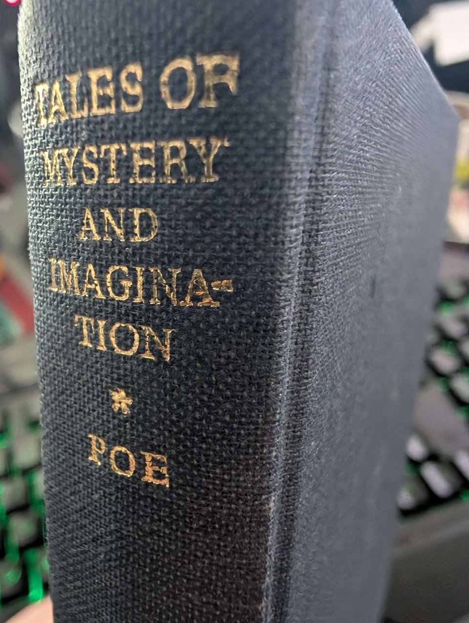 a close up of a blue-grey small hardback book with gold writing. Tales of Mystery and Imagination * Poe