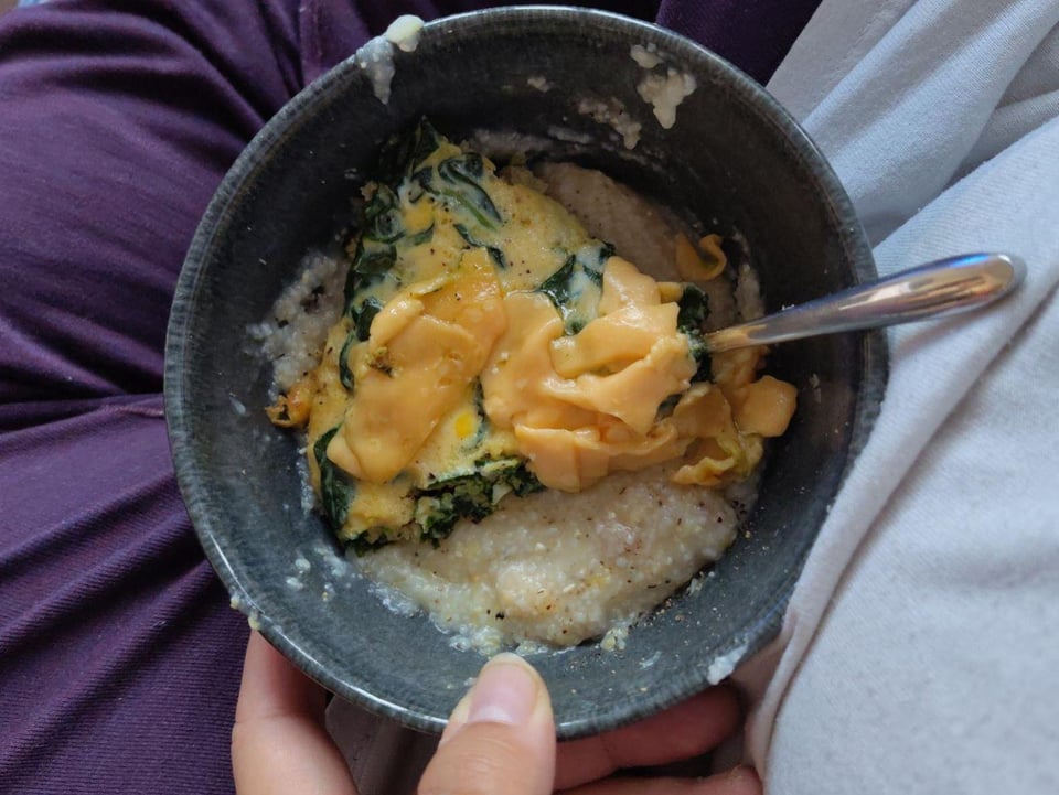 a top-down view of a bowl of grits and a slice of spinach omelette with slices of cheese on top
