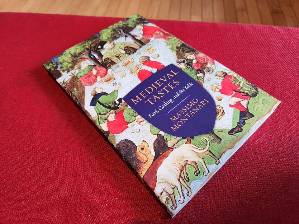 A paperback copy of Medieval Tastes by Massimo Montanari on a red ottoman.