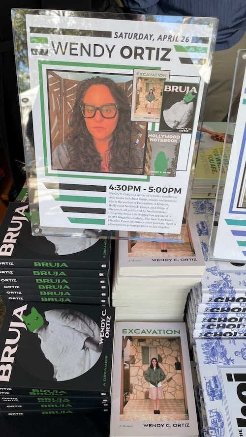 A photo of stacks of Excavation and Bruja by Wendy C. Ortiz with a placard on top of one stack announcing a book signing that day.