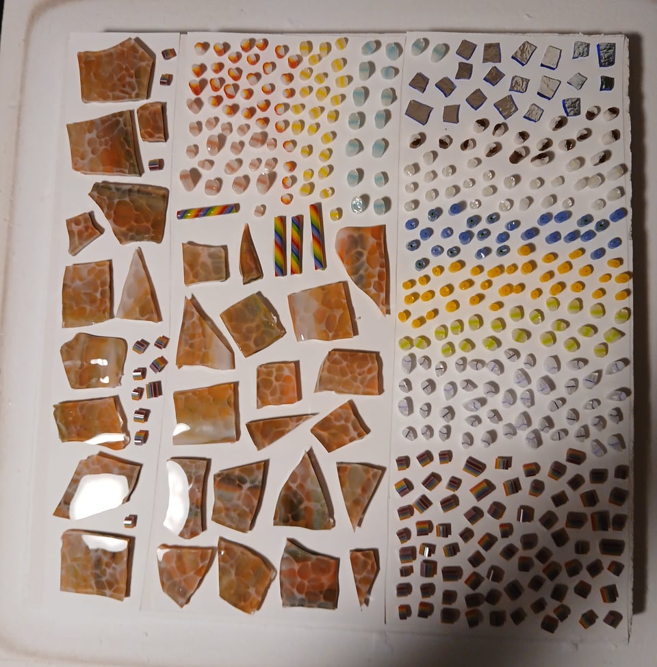 kiln shelf with a bunch of orange and green dragonskin pieces of glass and assorted rainbow murrine pieces, jellyfish murrine pieces, floral pieces and a few chopped up pieces of dichroic glass