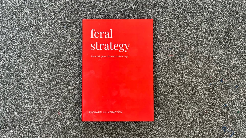 Photograph of a book. It has a plain red cover with white text, which says, "feral strategy". The subheading is, "Rewild your brand thinking". The author is Richard Huntington.