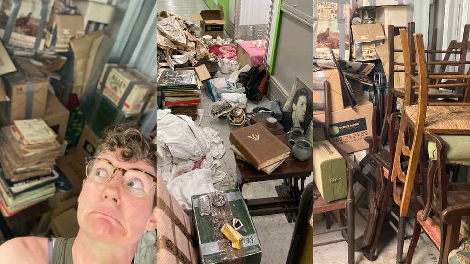 Lucy looking daunted by a huge collection of old cardboard boxes, wooden chairs, and messy piles of photographs.