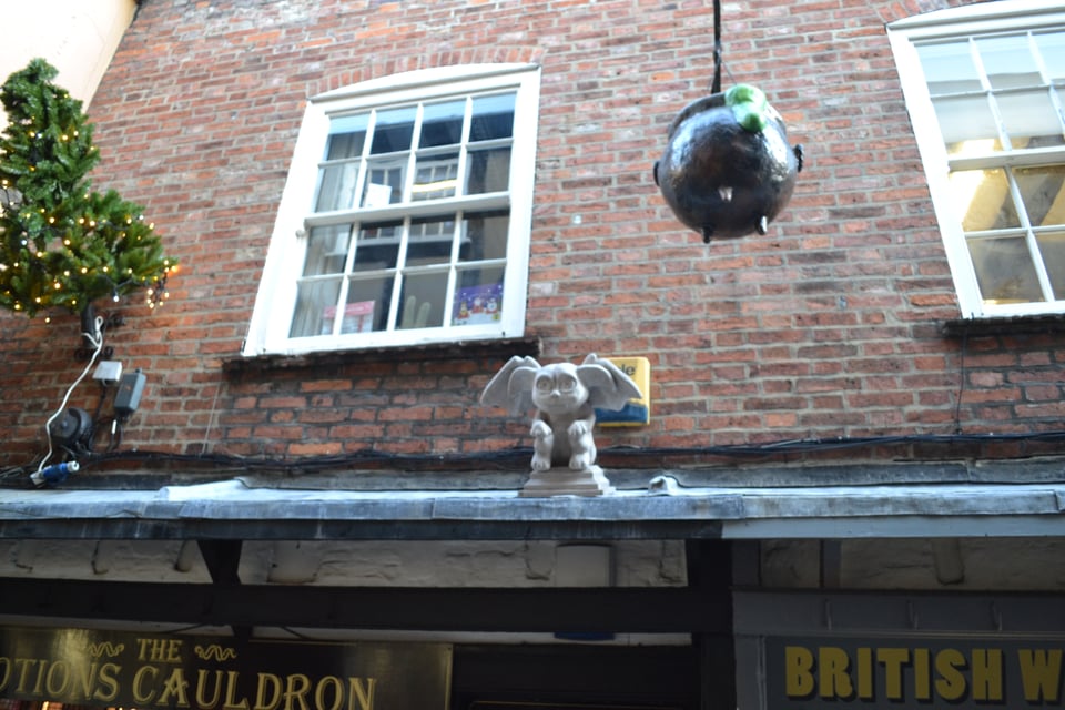 A brick building with a chibi gargoyle and a cauldron.