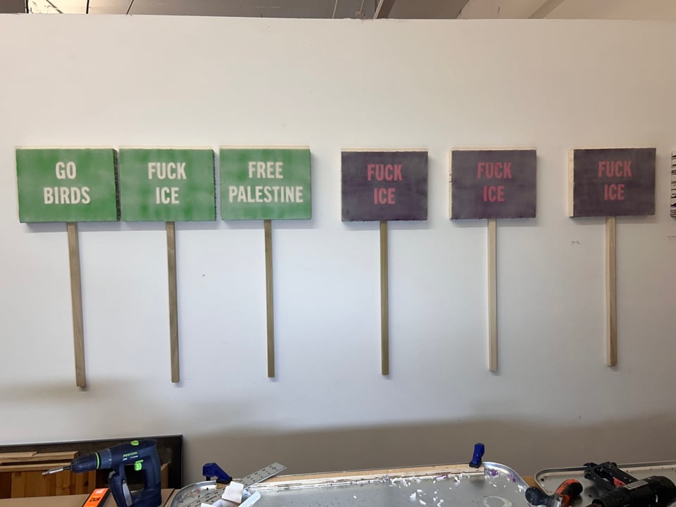 Wall of new paintings. Three green paintings that say GO BIRDS, FUCK ICE, and FREE PALESTINE. Three purple paintings that say FUCK ICE. All the paintings have sticks attached so they look like protest signs.