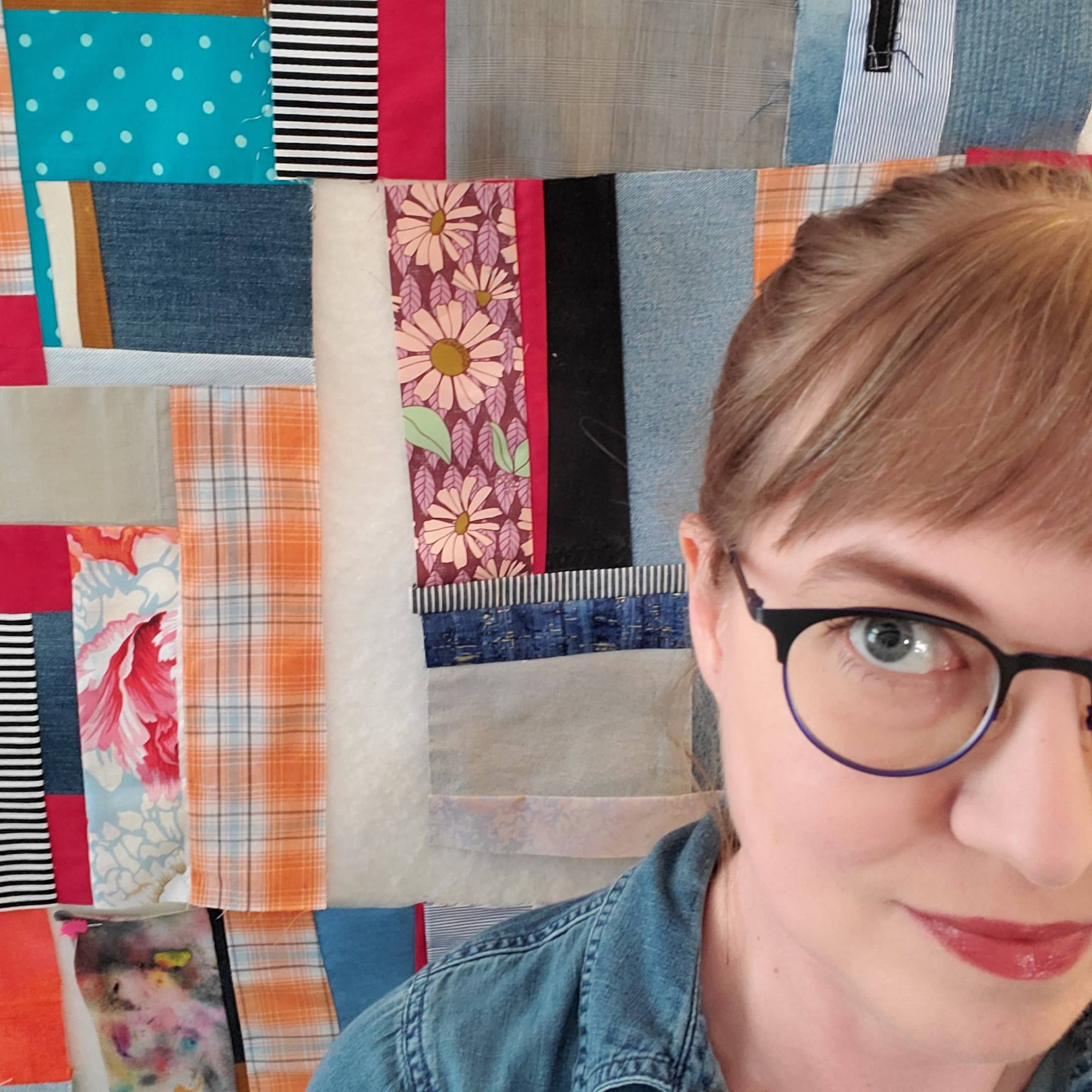 Selfie of Sarah sitting in front of her design wall with a patchwork quilt in progress.